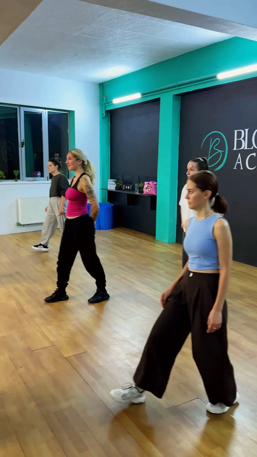 Cursante Street Dance Lady Only pășesc prin sala BloomArt Academy, în fața peretelui cu sigla școlii