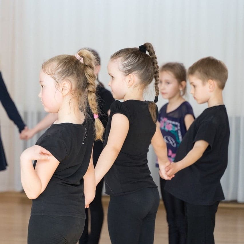 Children in dance outfits, sitting in a row and watching the exercise