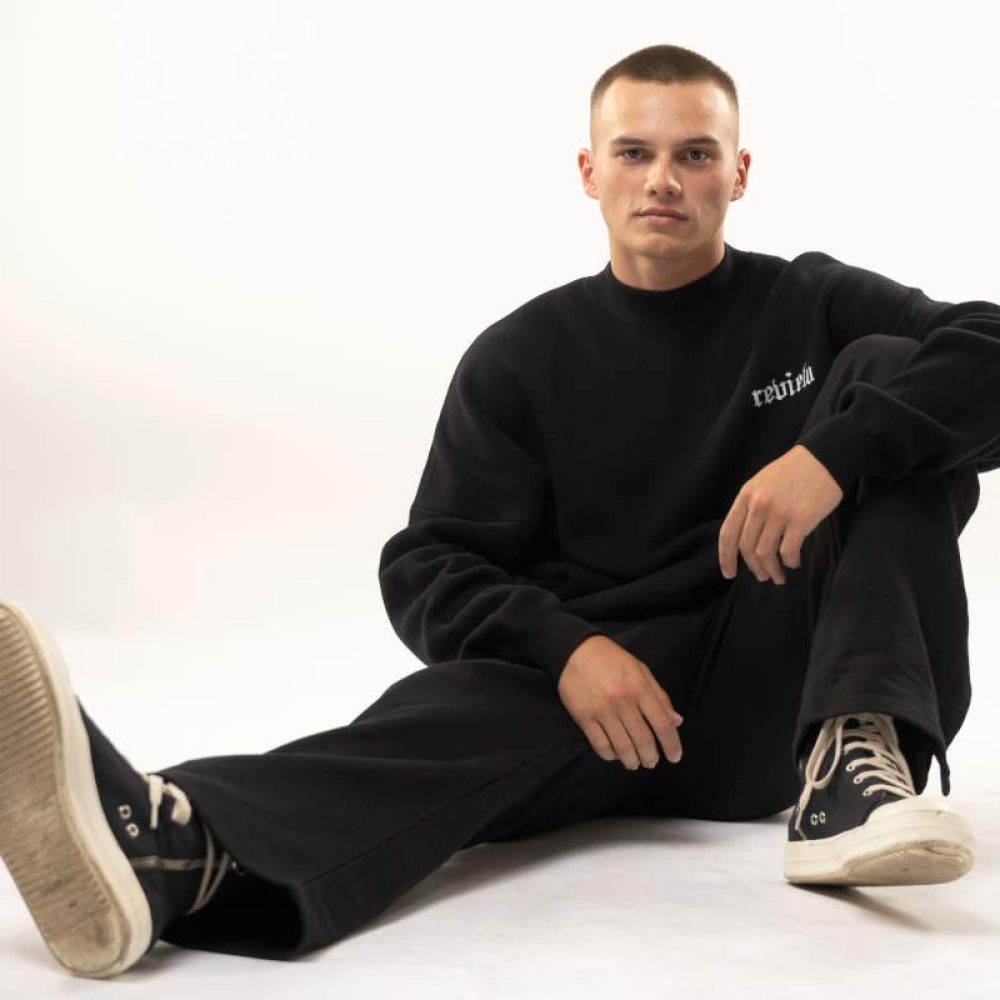 Dancer in a black outfit and sneakers, sitting on the floor